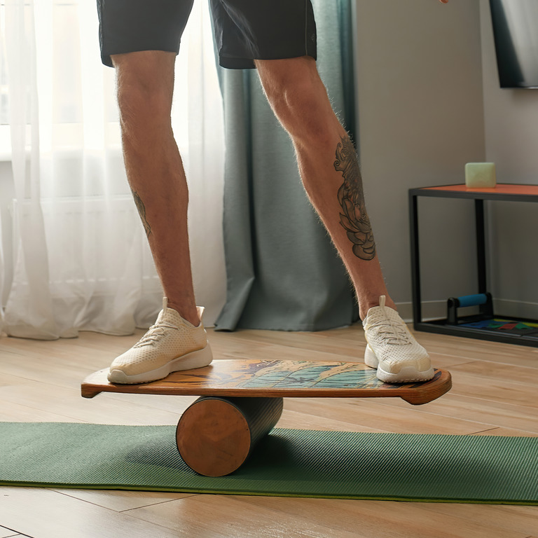Junger Mann surft auf Balance Board zuhause auf Yogamatte
