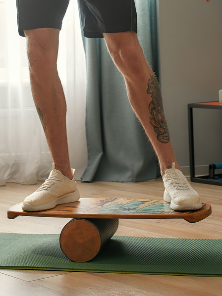 Mann surft auf Balance Board auf Yogamatte im Wohnzimmer