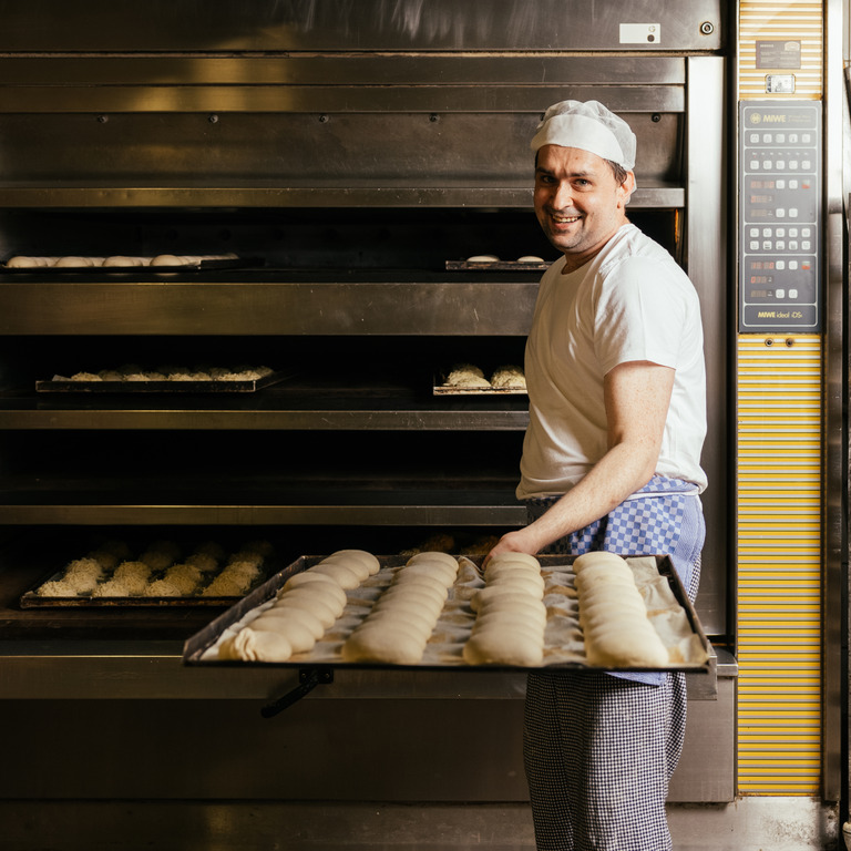 Bäcker in Goldbrötchen Bäckerei holt Brötchen aus dem Ofen