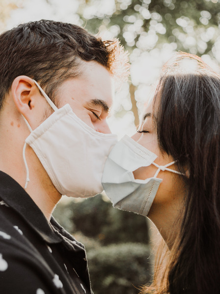 Mann und Frau mit medizinischen Masken deuten Kuss an