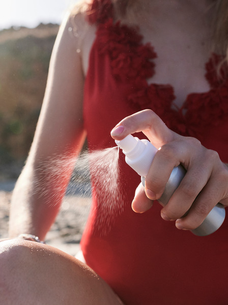 Frau im roten Badeanzug mit Sonnenallergie sprüht sich ein