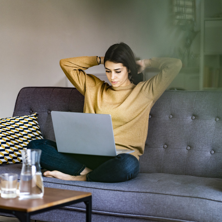 Junge Frau sitzt auf Sofa und übt am Computer Microjob aus