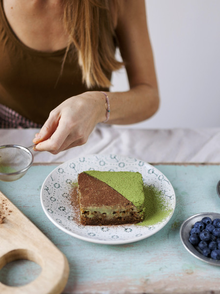 Frau dekoriert veganen Kuchen mit Matcha und Kakaopulver