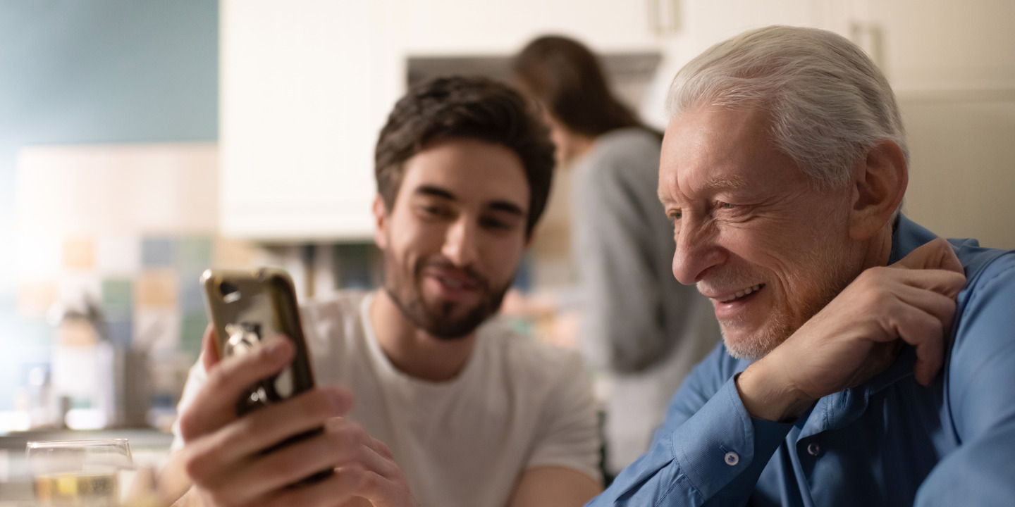 Junger Mann zeigt älteren Herren etwas auf seinem Smartphone.