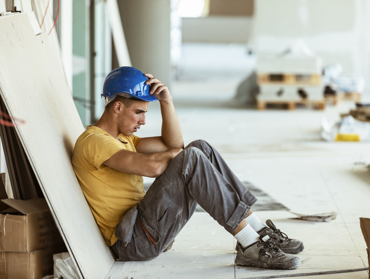Handwerker mit Burnout sitzt niedergeschlagen am Boden