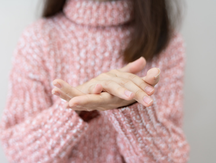 Frau im rosa Pulli legt Hände mit gepflegten Nägeln aufeinander 