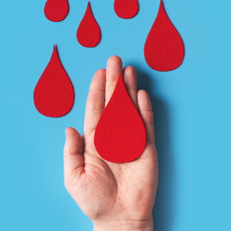 Bluttropfen aus rotem Filz auf Hand vor blauem Hintergrund