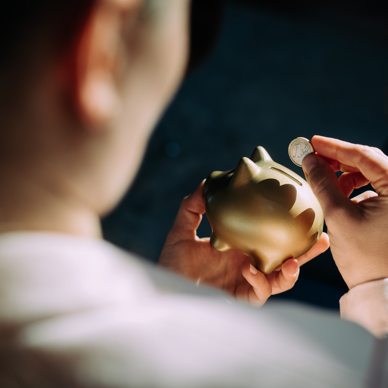 Person steckt 1-Euro-Münze in Sparschwein