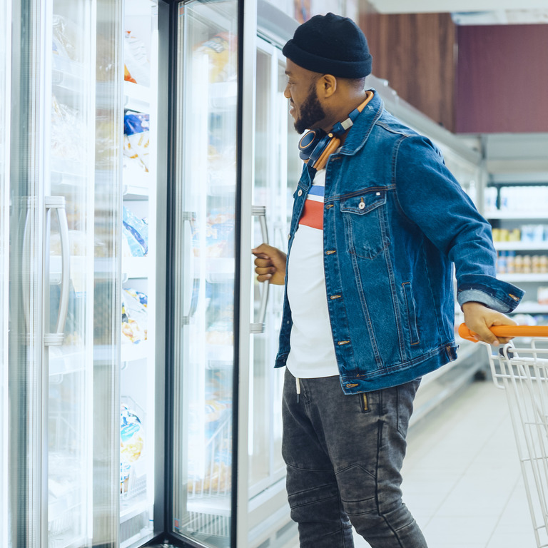 Mann im Supermarkt mit Einkaufswagen öffnet Kühlregal
