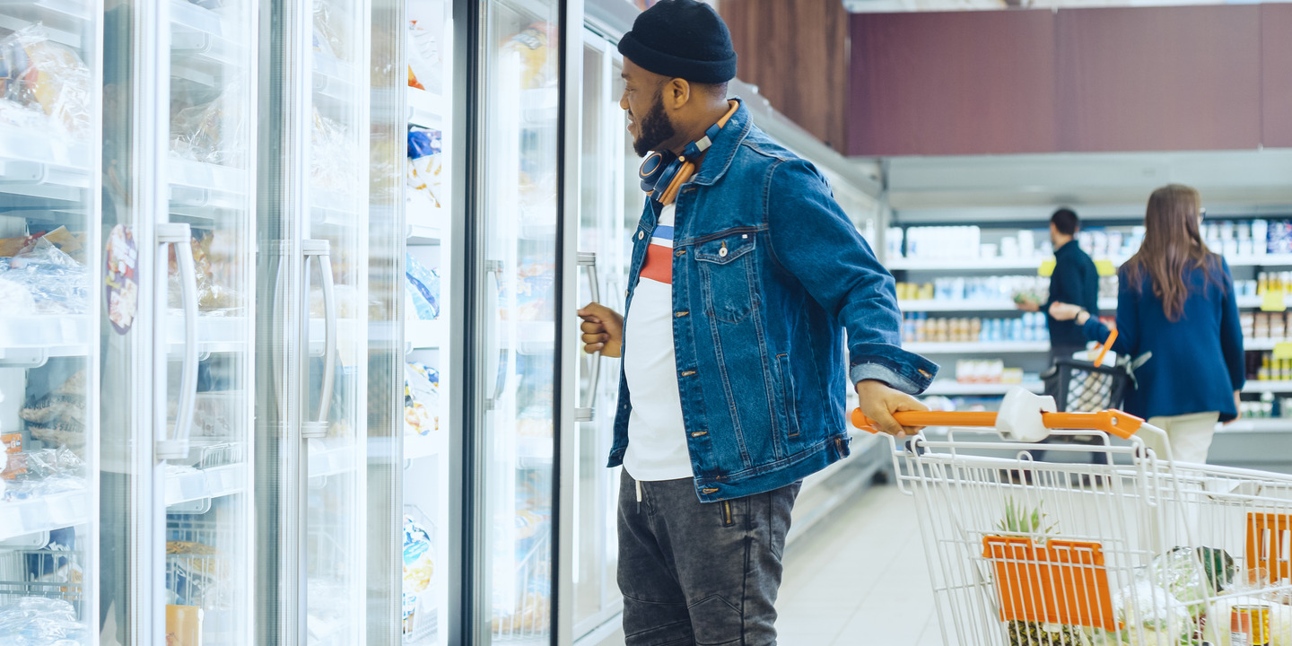 Mann mit Einkaufswagen steht vor Regal im Supermarkt