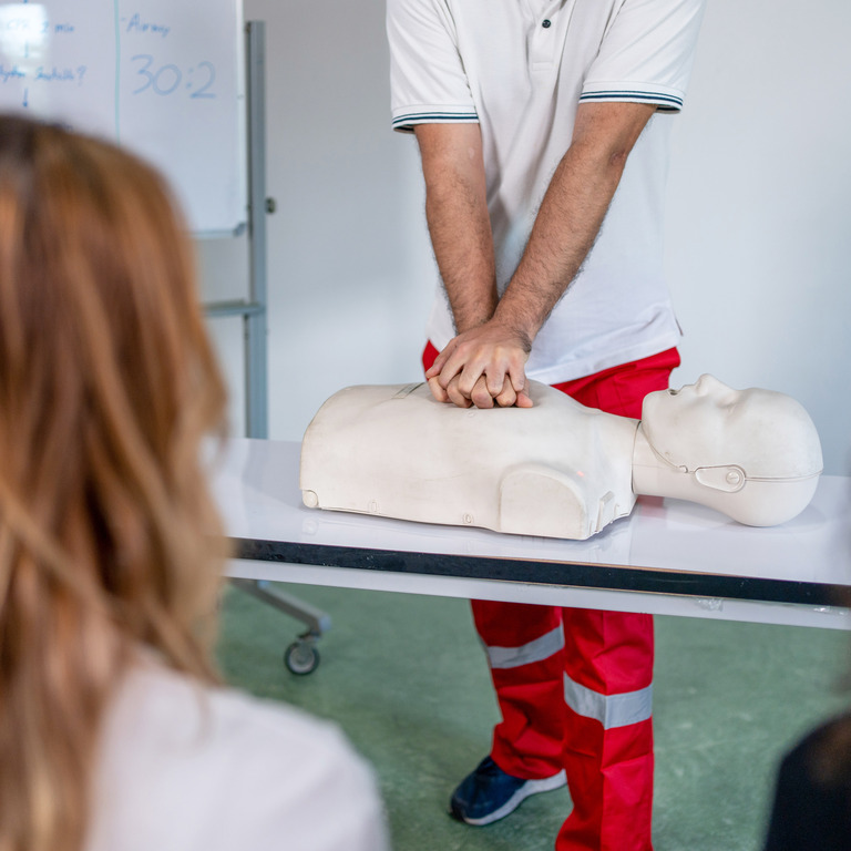 Ein Sanitäter zeigt Teilnehmerinnen die Herzdruckmassage an einer Übungspuppe.