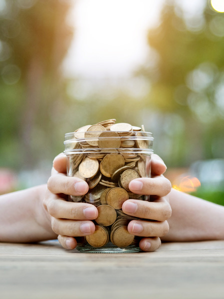 Frau hält Einmachglas voller Münzen mit den Händen fest
