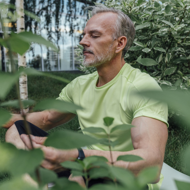 Mann mit geschlossenen Augen meditiert zwischen Pflanzen