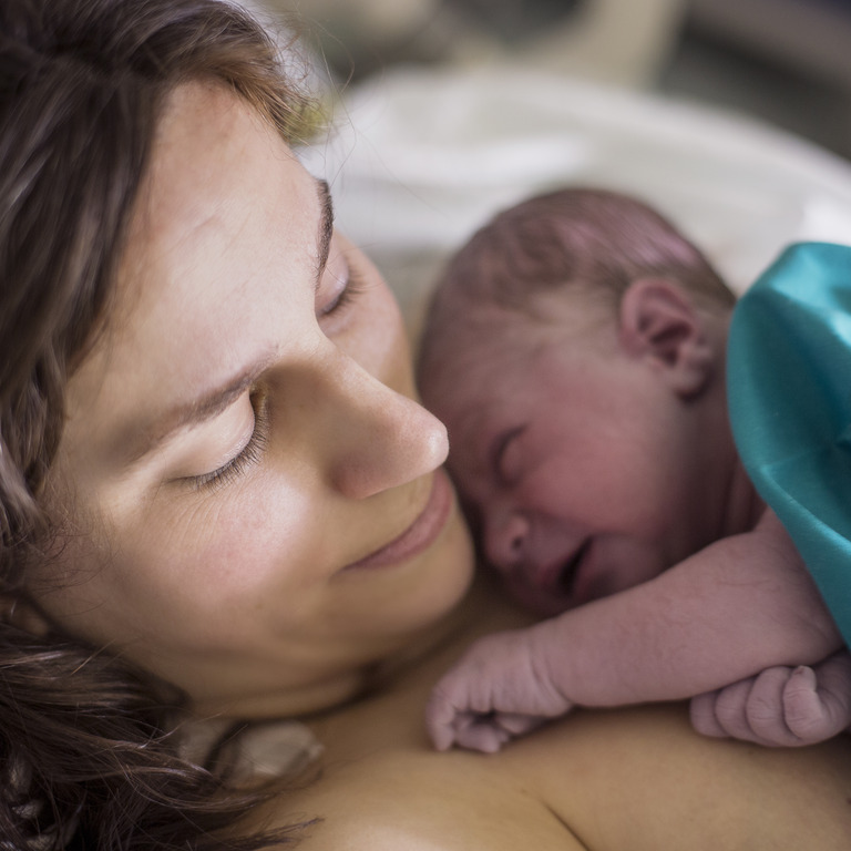 Frau mit ihrem Neugeborenen auf dem Arm nach der Entbindung