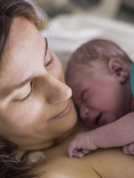 Frau mit ihrem Neugeborenen auf dem Arm nach der Entbindung