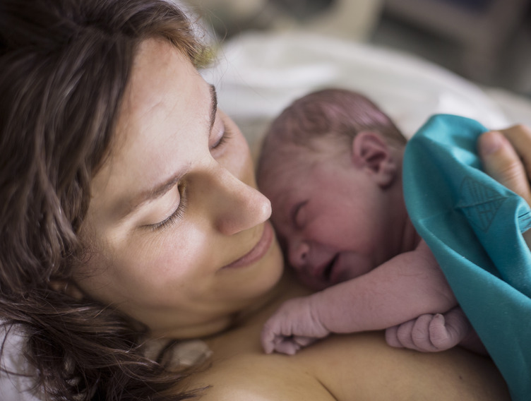 Frau mit ihrem Neugeborenen auf dem Arm nach der Geburt