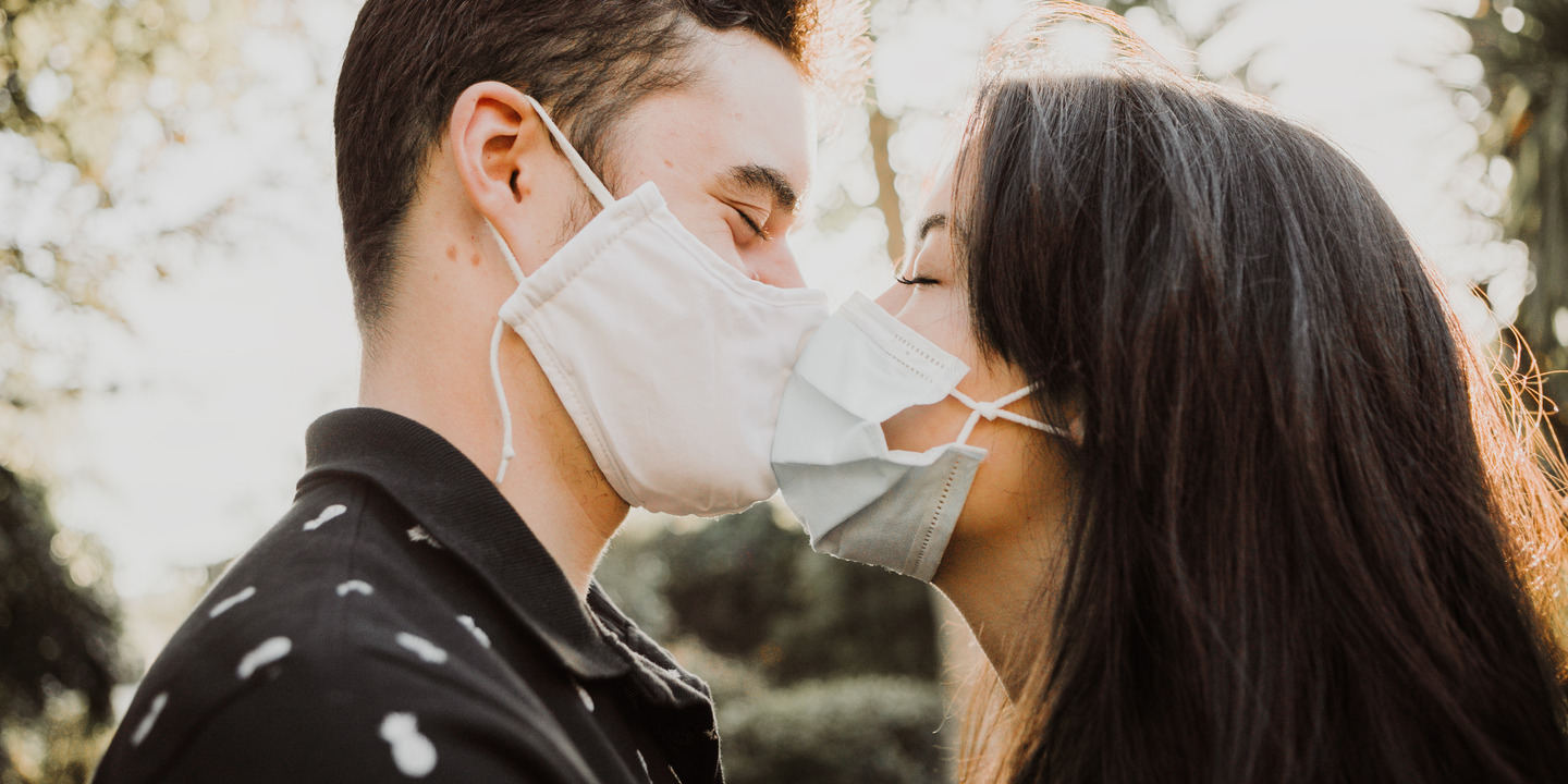 Mann und Frau mit medizinischen Masken deuten Kuss an