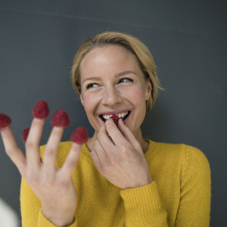 Frau isst Himbeeren von ihren Fingern.
