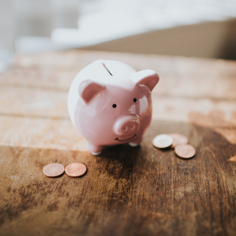 Rosanes Sparschwein steht umgeben von Geldmünzen auf einem Holztisch