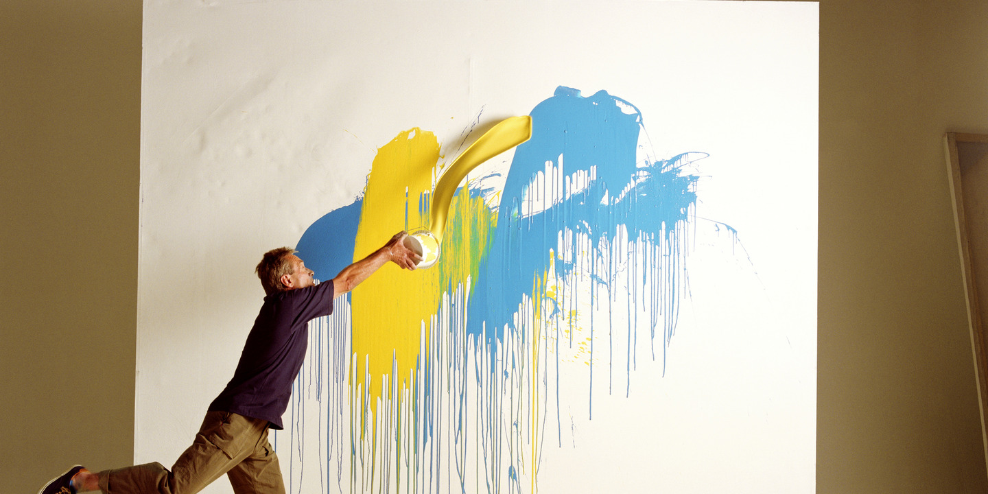 Mann spritzt Farben an eine große Leinwand