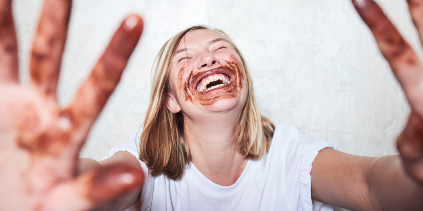 Frau lacht herzhaft schokoladenverschmiert in Gesicht und Händen