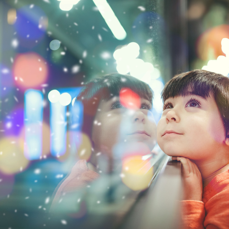 Kind schaut durch Fensterscheibe auf unscharfe Lichter