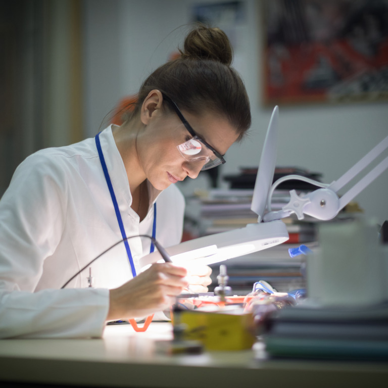 Frau im Laborkittel beugt sich über ein Mikroskop