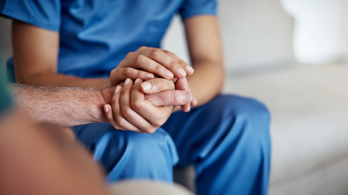 Pfleger hält die Hand eines alten Patienten
