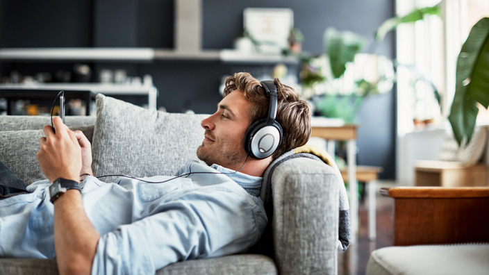 junger Mann liegt entspannt auf einer Couch und hört über seine Kopfhörer die Tinnitracks-App