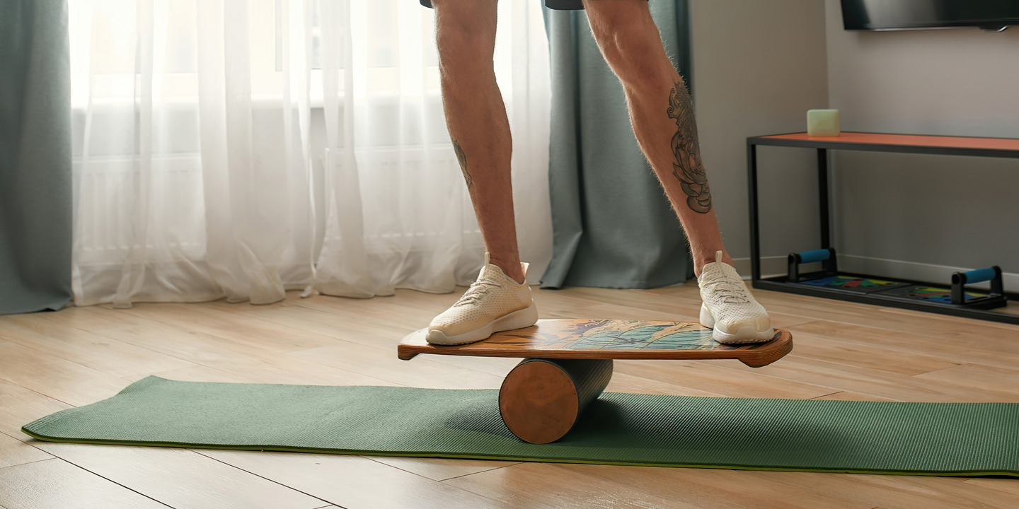 Mann trainiert auf Balance Board auf Yogamatte im Wohnzimmer