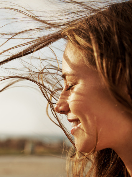 Frau mit wehendem Haar genießt den Wind und frische Luft