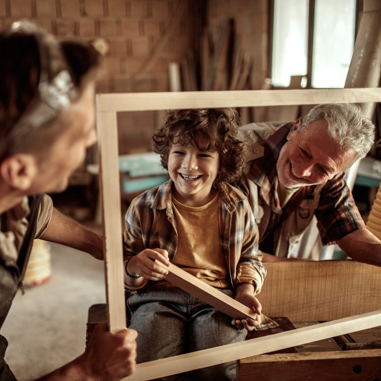 Großvater, Vater und Sohn halten lachend einen Holzrahmen fest
