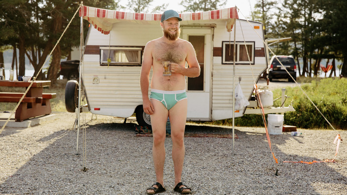 Junger Mann mit Bart steht in Unterhose vor seinem Wohnwagen
