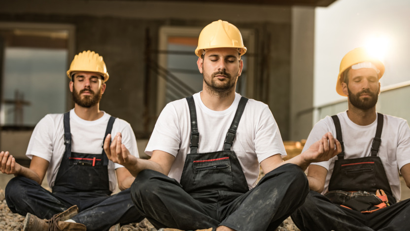Männer in Baustellenkleidung machen eine Yogaübung