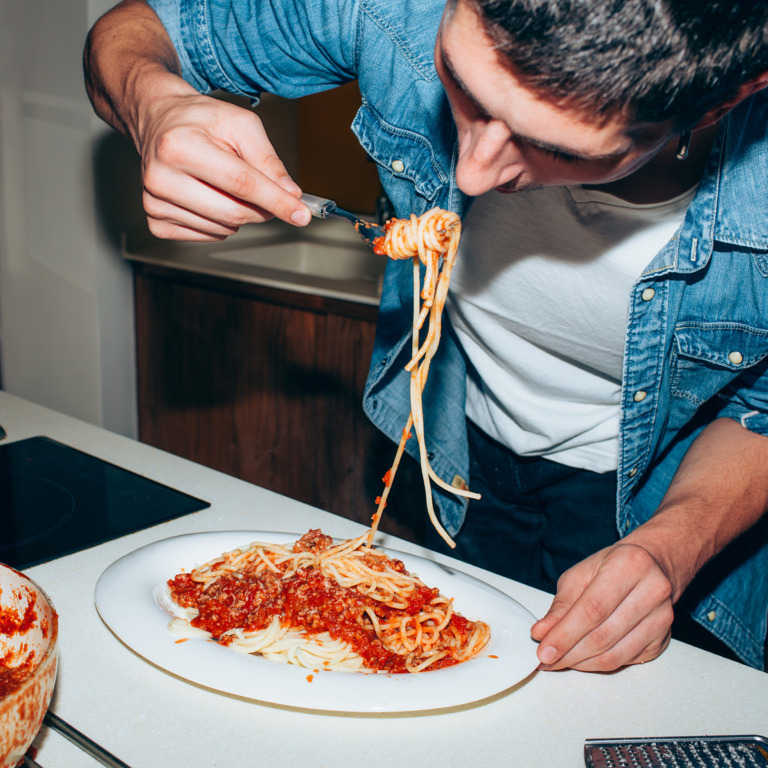 Student isst Spaghetti mit Tomatensoße im Stehen
