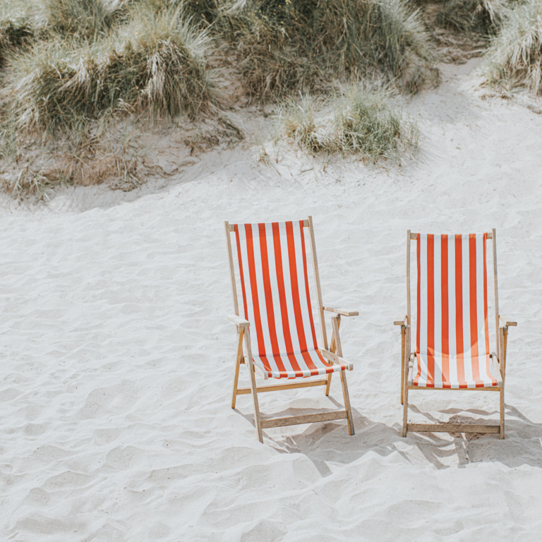 Zwei leere Liegestühle am Strand.