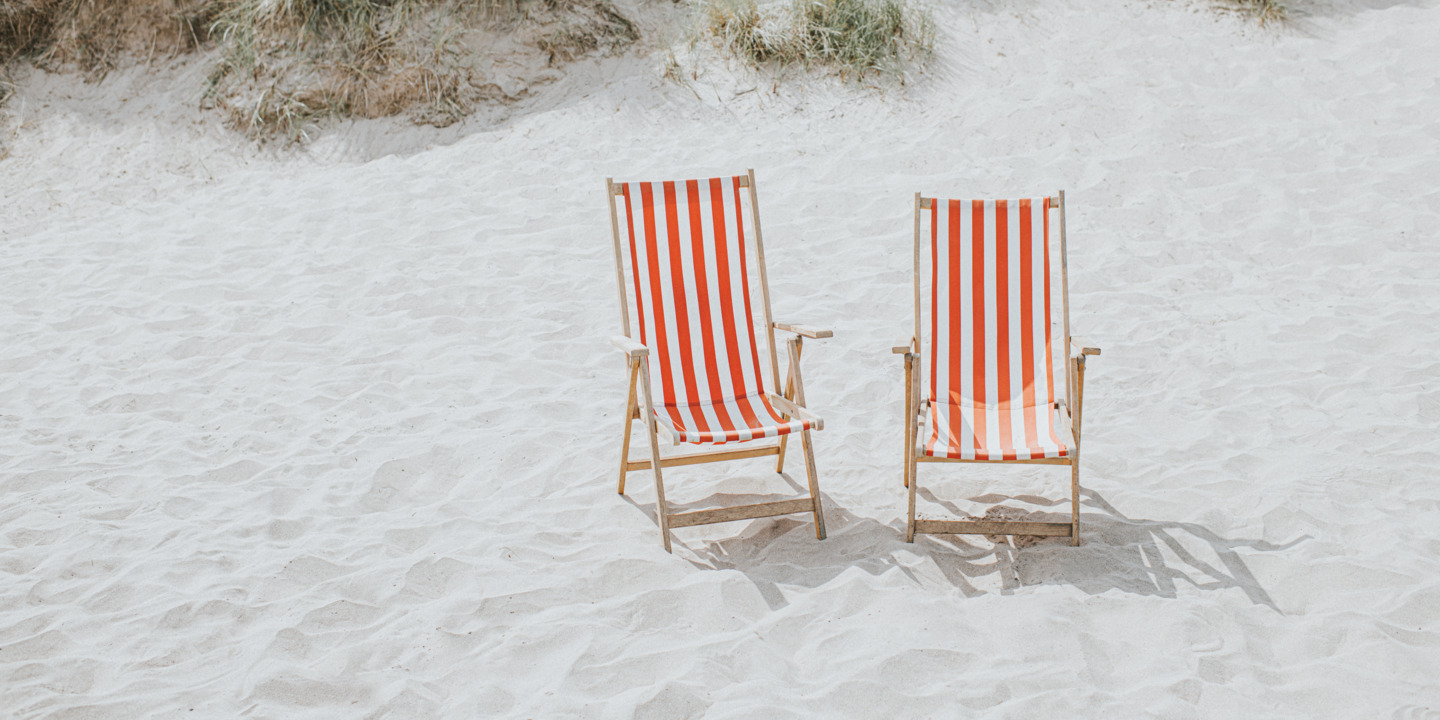 Zwei leere Liegestühle am Strand.