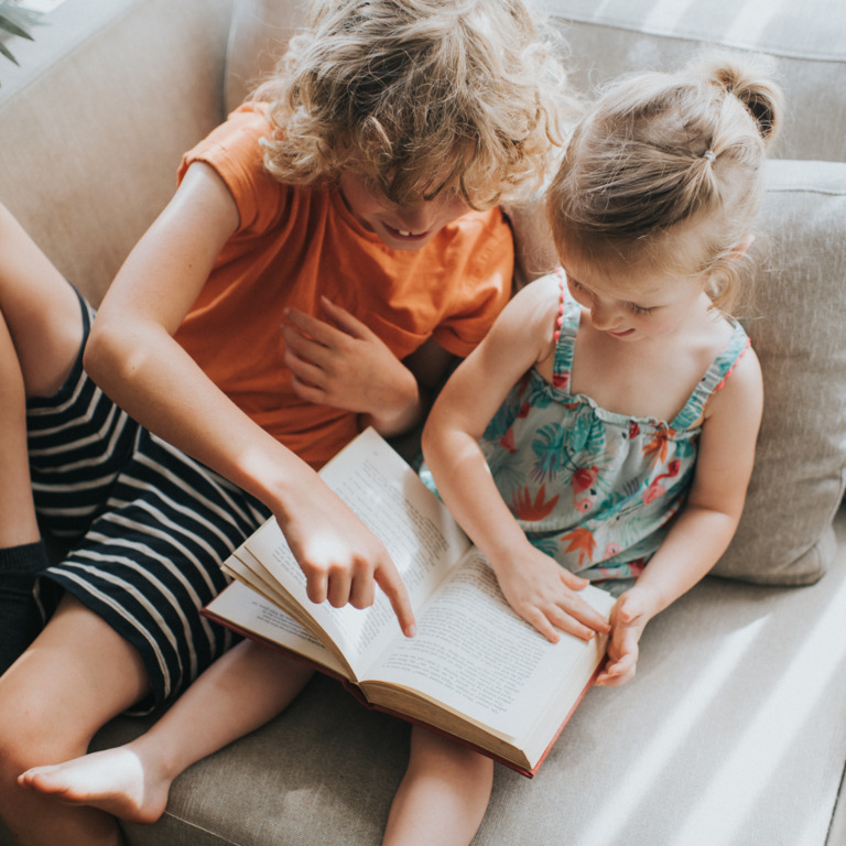 Zwei Kinder sitzen auf dem Sofa und lesen zusammen ein Buch