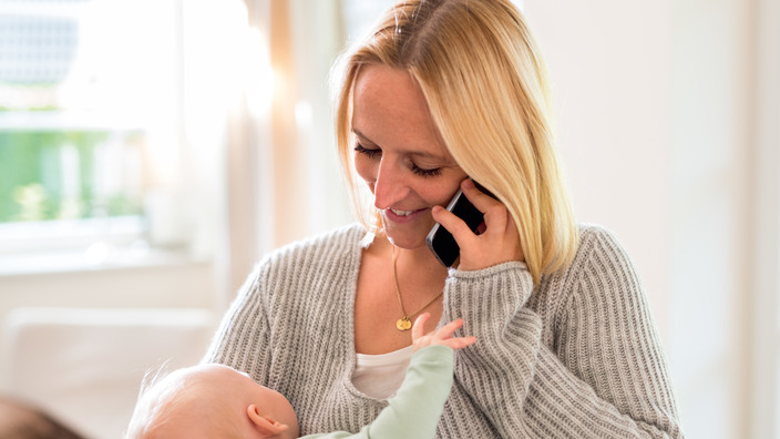 Frau hält ihr Baby im Arm und telefoniert