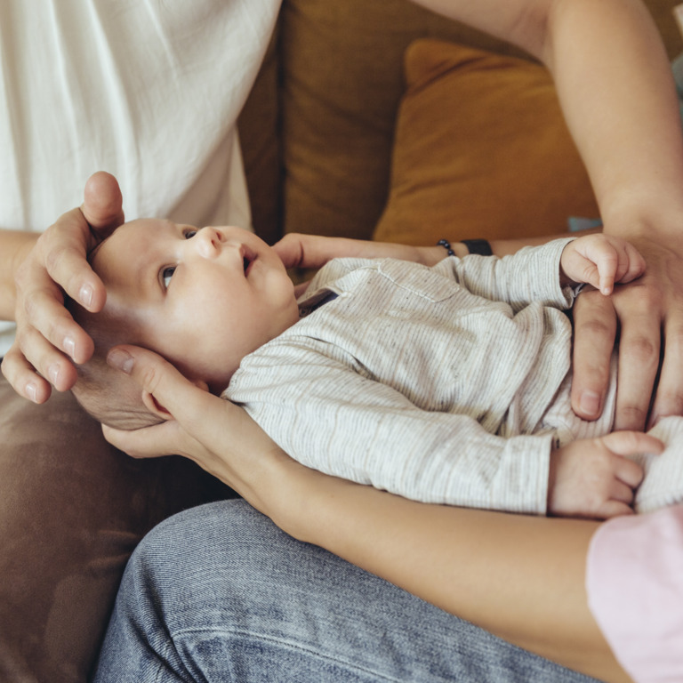 Mutter hält Neugeborenes und Hebamme untersucht es