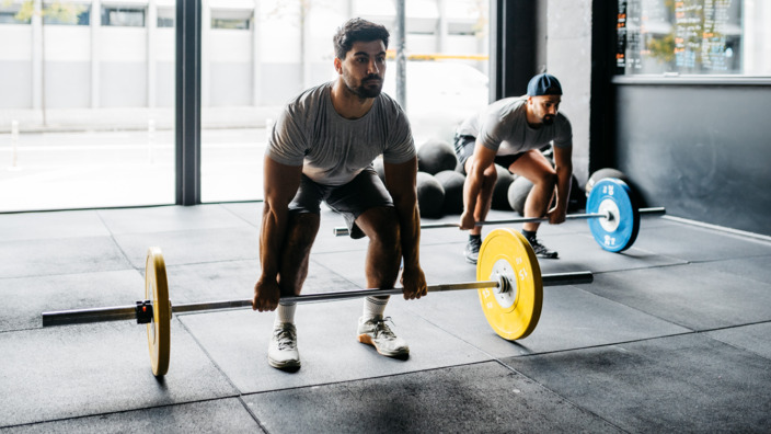 Zwei Männer im Fitnessstudio, die in der Hocke stehen und mit Gewichten trainieren