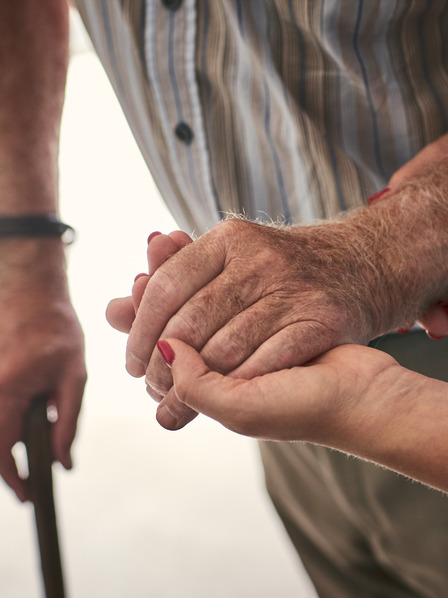 Pflegekraft stützt den Arm eines älteren Mannes mit Gehstock