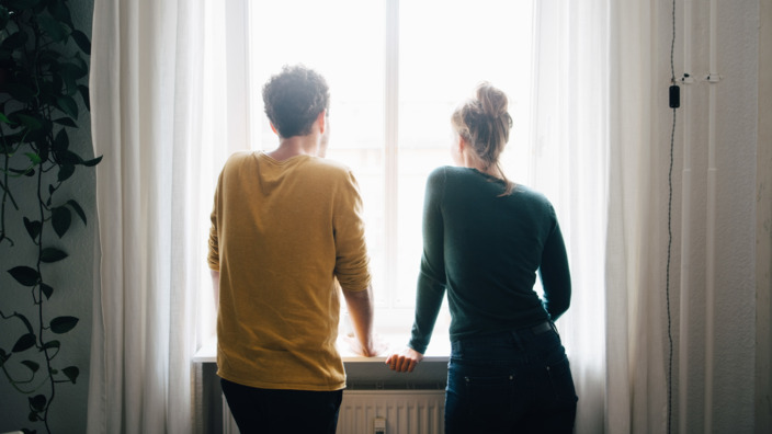Rückenansicht eines jungen Paares, das aus dem Fenster schaut