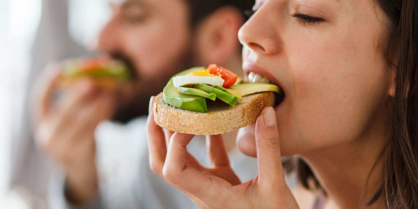 Frau und Mann beißen in belegtes Brot mit Avocado