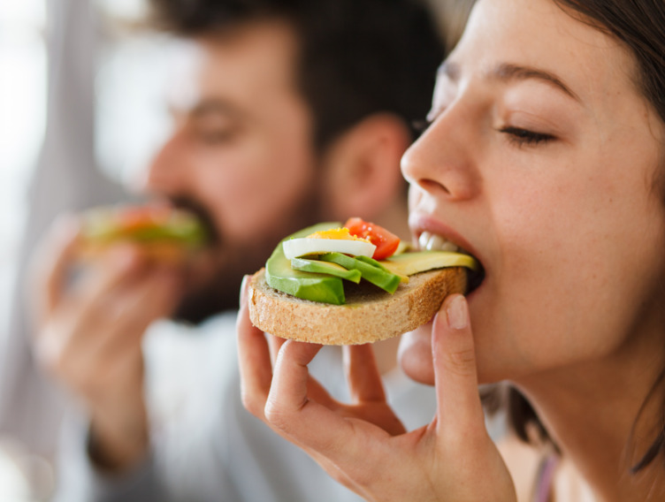 Frau und Mann beißen in belegtes Brot mit Avocado