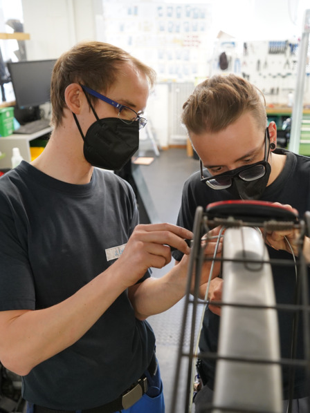 Vielfalt in der Fahrradwerkstatt: Zwei junge Erwachsene mit unterschiedlichem Hintergrund reparieren gemeinsam ein Fahrrad.