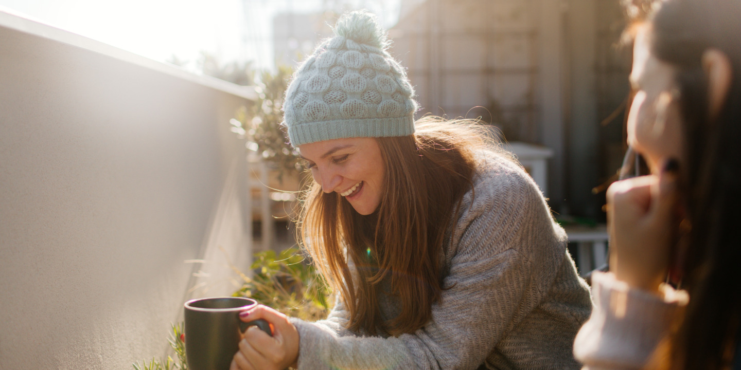 Zwei Frauen sitzen lachend am Balkon in der Sonne