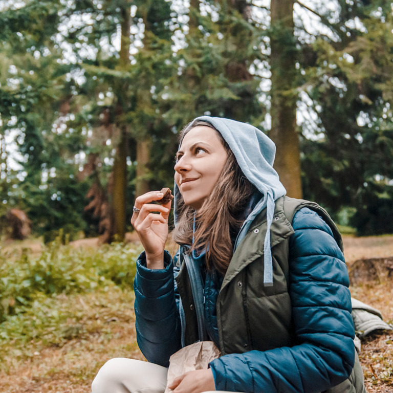 Frau mit Herbstjacke macht beim Wandern eine Pause und isst gesunden Proviant.