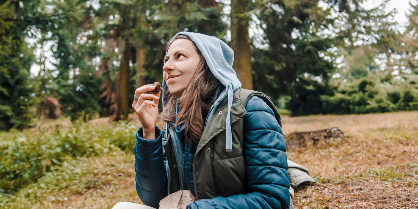 Frau macht im Wald beim Wandern eine Essenspause mit dem Proviant aus ihrem Rucksack.