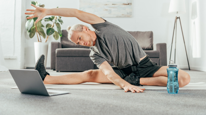 Mann in Sportkleidung macht Fitnessübungen vor einem Laptop